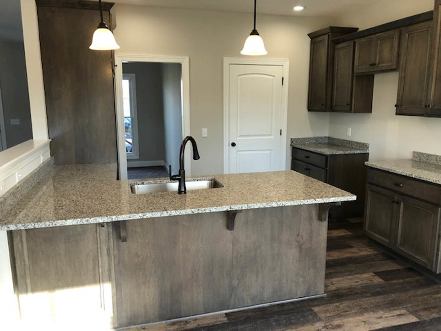 Granite island with undermount sink and chrome faucet, white cabinetry with black handles, stainless steel appliances, tile backsplash, and pendant lighting in a modern kitchen
