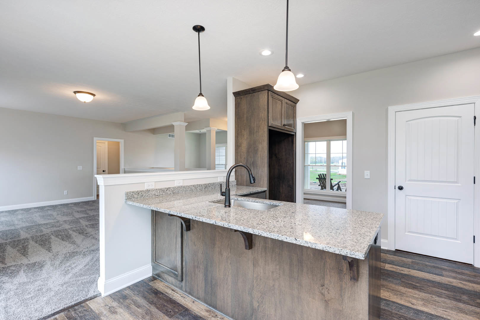 Open kitchen with wood flooring, granite countertops, stainless steel sink, white cabinetry, and tile backsplash; white door with black handle visible in background.