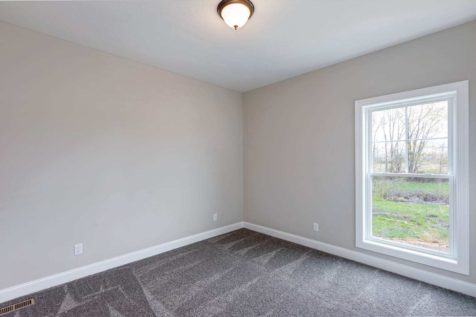 Room with grey carpet, white walls, ceiling light fixture with round shade, large window showing grass and trees outside