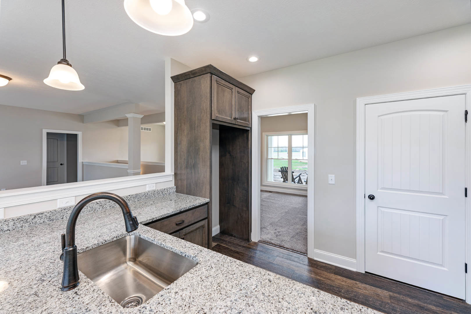 Modern kitchen featuring a stainless steel sink with chrome faucet, white tile backsplash, wall-mounted mirror, white cabinetry, black door knob, and globe-shaped light fixture