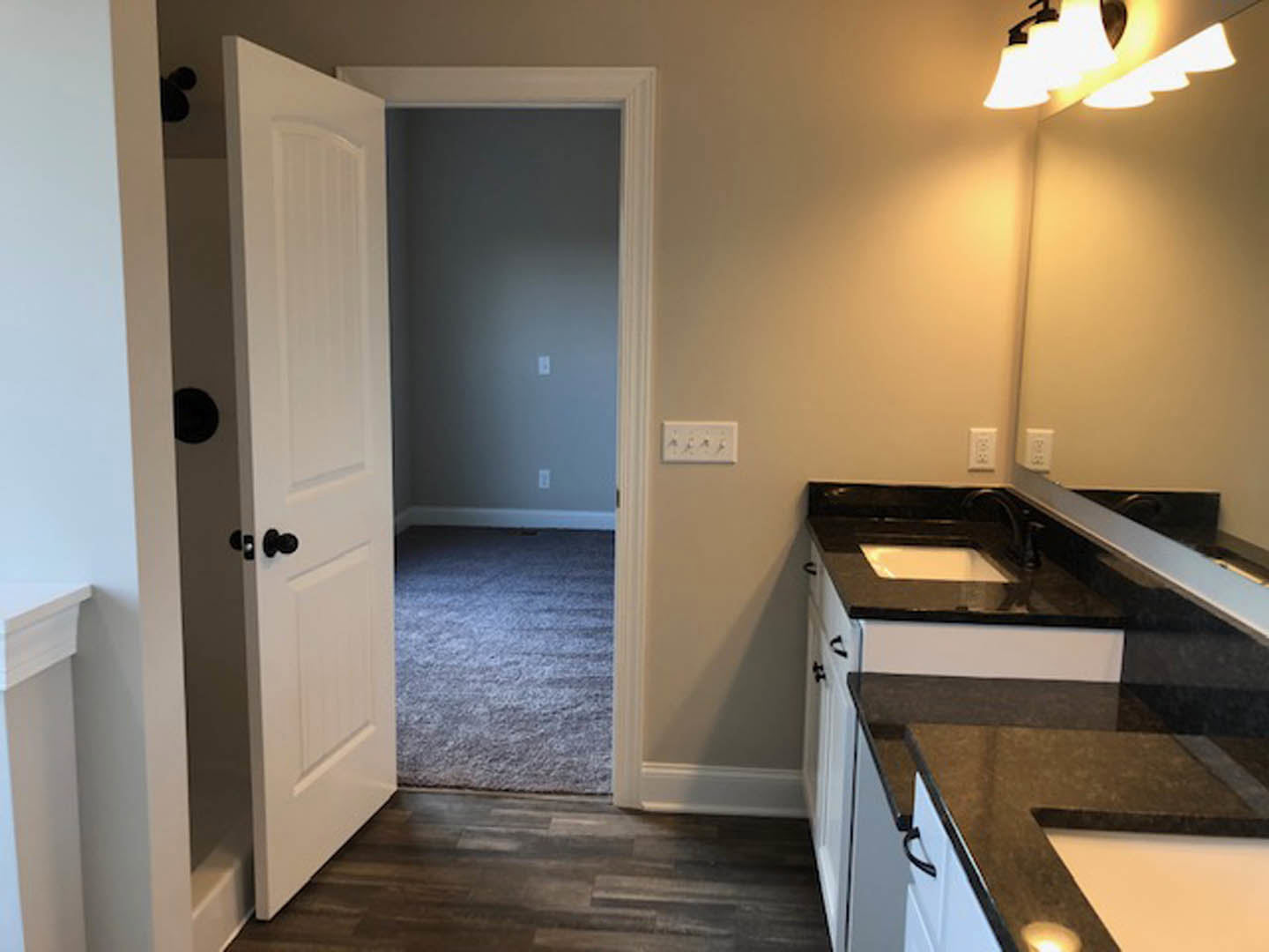 Bathroom with open white door, wood floor with patterned rug, light grey countertop, white cabinetry, and tile backsplash.