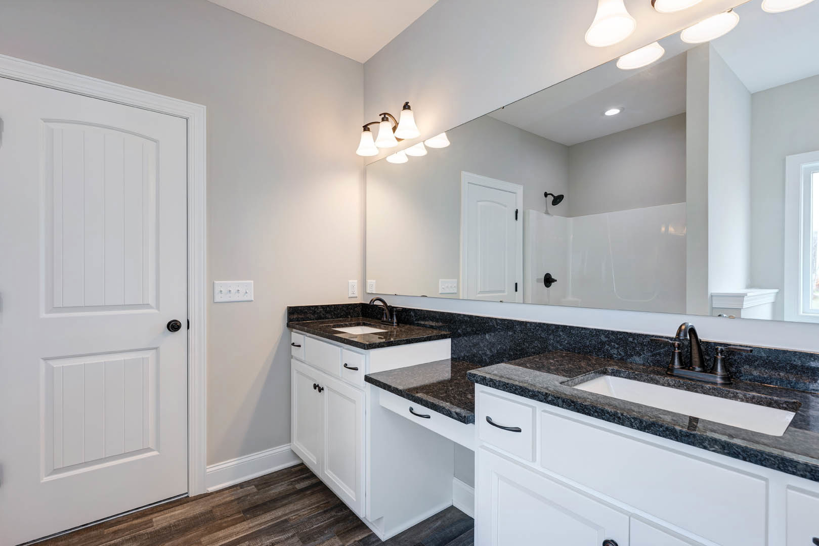 Bathroom with double white sinks, wide rectangular mirror, light gray tile backsplash, white cabinetry with black hardware, chrome faucets, and white painted door with black knob