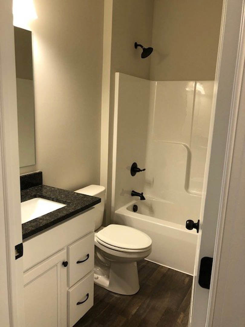 White porcelain toilet with closed seat next to rectangular sink on stone countertop, light tile flooring, wall-mounted mirror above sink, chrome faucet and towel ring visible.