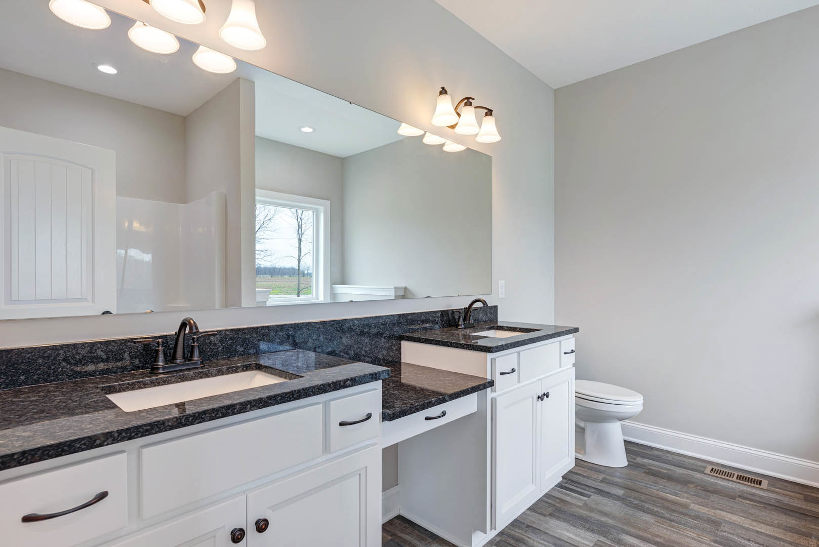 Bathroom featuring black granite countertop, rectangular mirror above white sink, white toilet, tile flooring, window with view of trees, and white door.