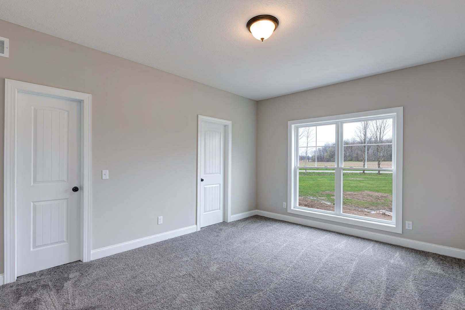 Bright room with white walls, ceiling light fixture, white door with black handle, large window overlooking grassy field, light-colored flooring, simple molding