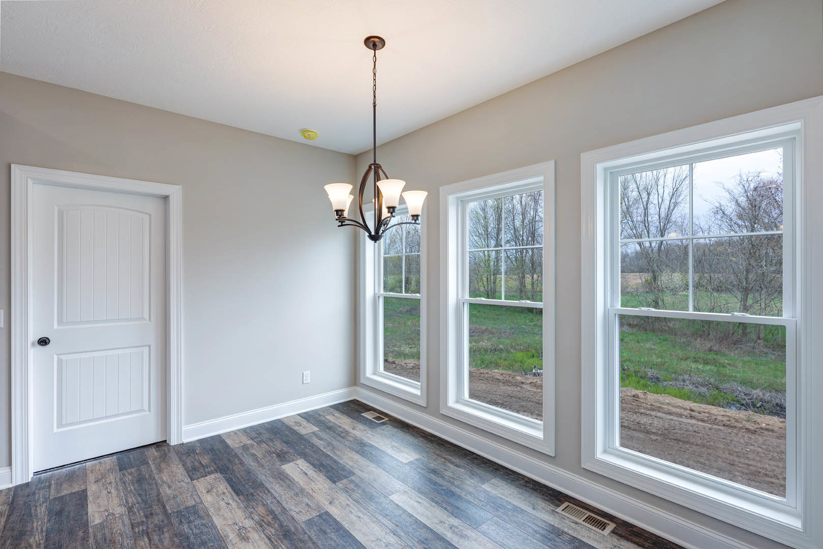 Chandelier with glass shades hanging from a white ceiling, large windows with black trim, white paneled door with black handle, hardwood flooring, crown molding, and views of a