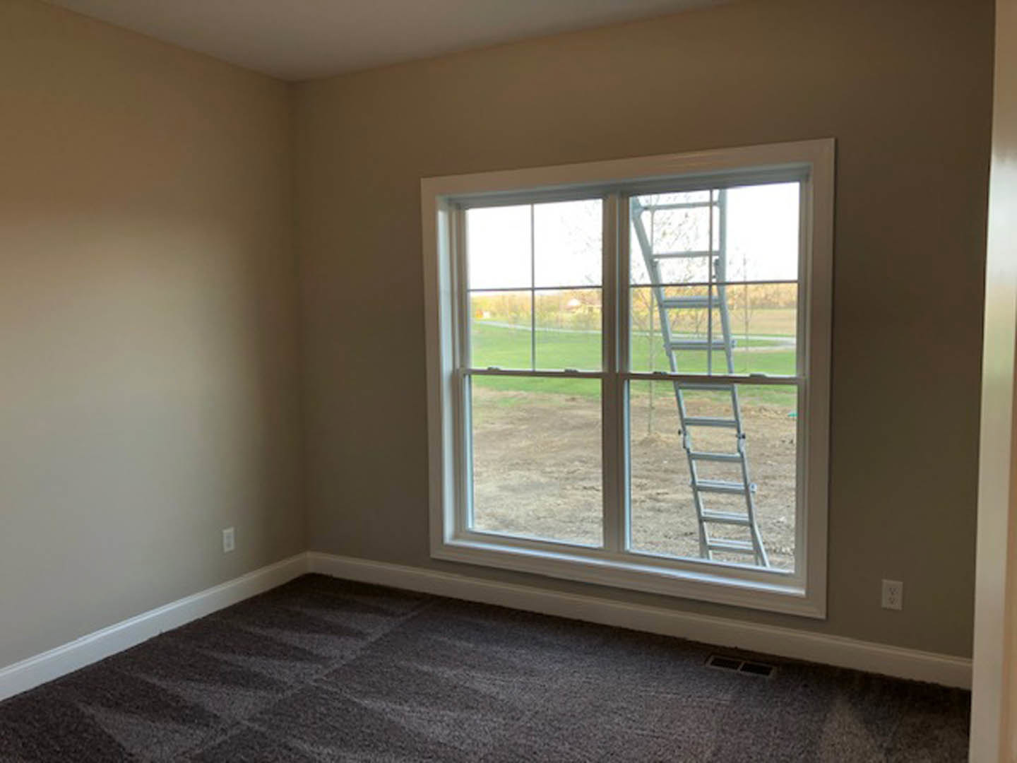 Ladder leaning against large window, white wall with brown trim, carpeted floor in custom home interior