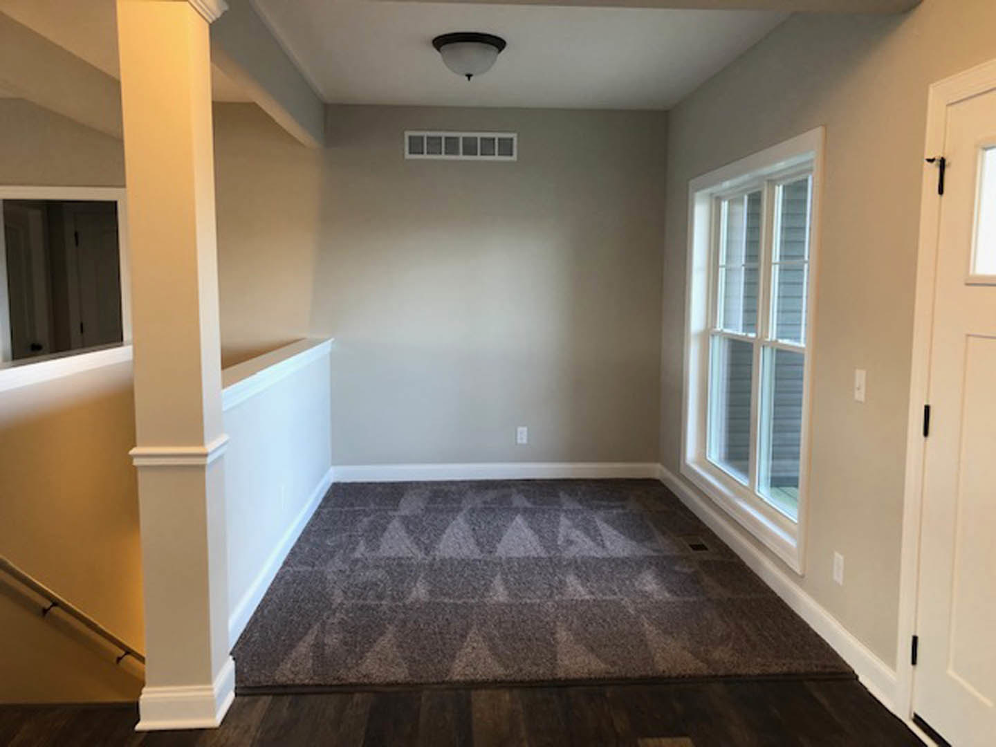 Carpeted bedroom with geometric patterned rug, white door, large window, and crown molding ceiling