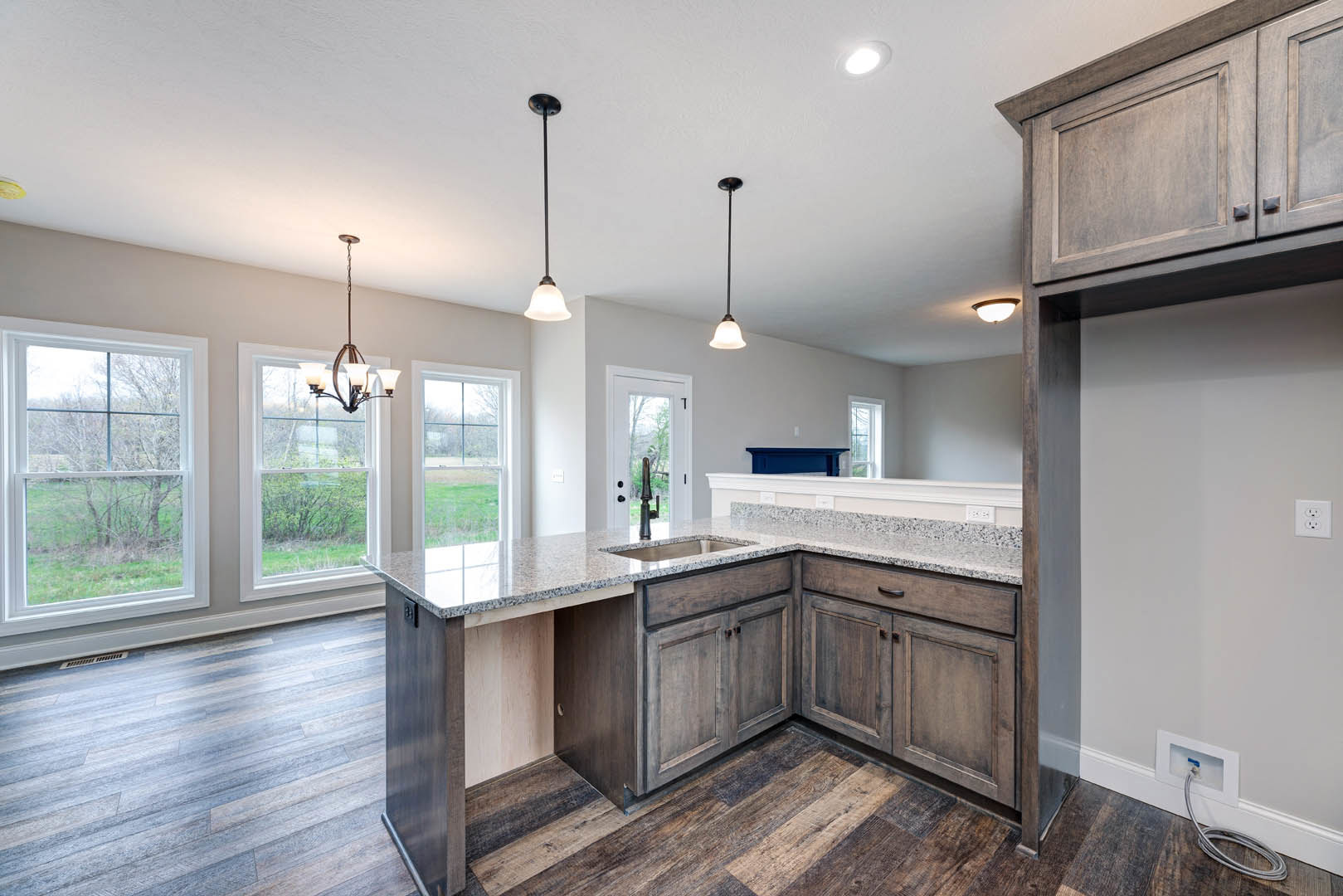 Marble countertop kitchen with tile backsplash, white cabinetry, stainless steel sink, ceiling light fixture with white shade, window overlooking outdoors, black pole lamp, white