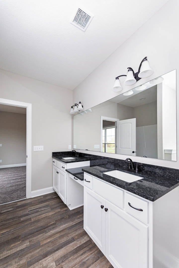 Bathroom with expansive mirror above white cabinets, wood flooring, white bathtub set on countertop, ceiling vent, and light fixture with white shade.