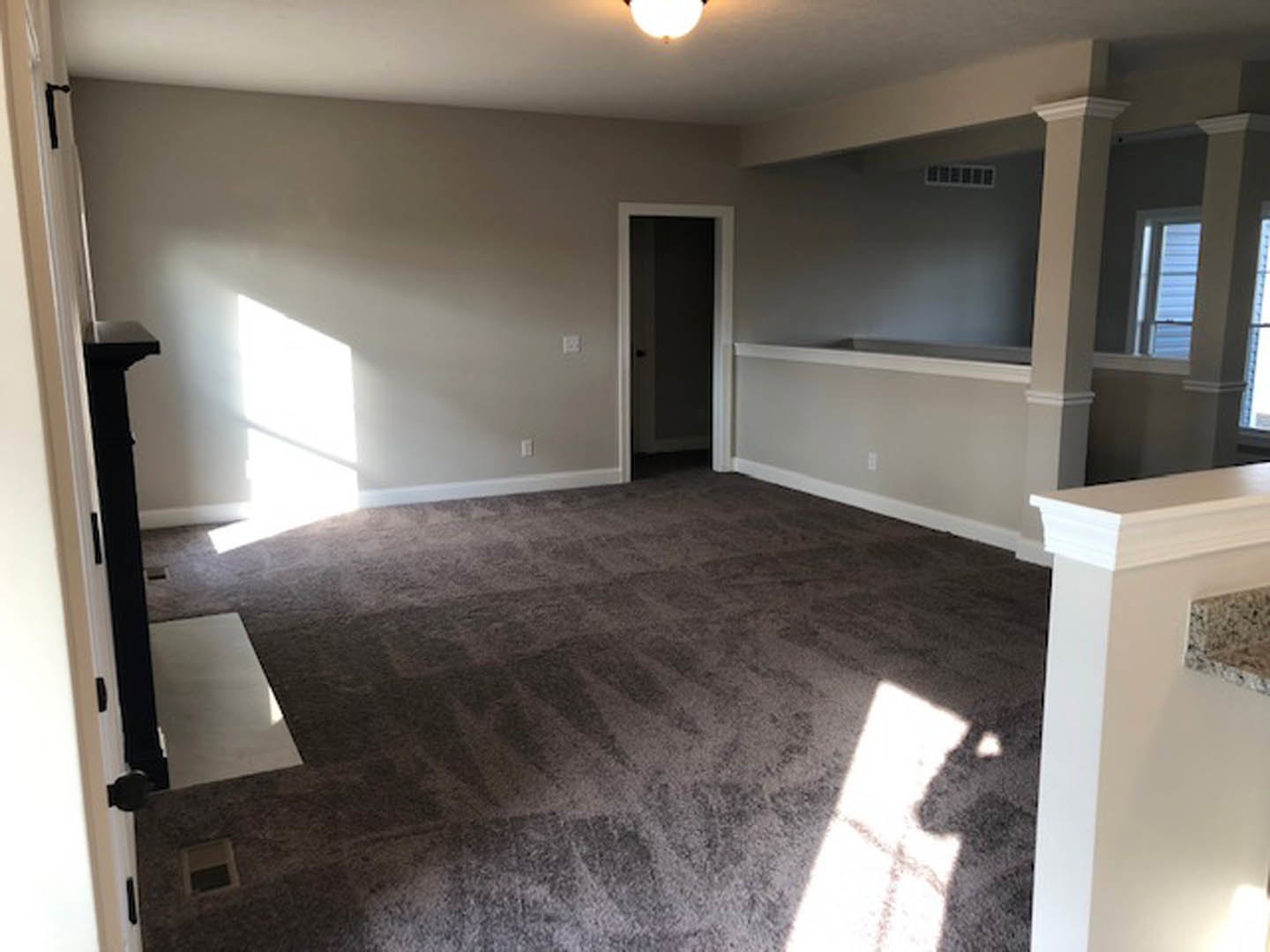 Carpeted living room featuring a wall-mounted TV, recessed ceiling light, white walls, marble countertop in the corner, open door, and window with natural light.