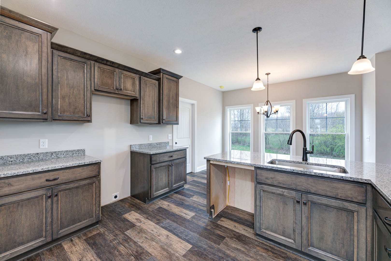 Kitchen with dark wood cabinets, polished granite countertops, stainless steel sink, tile backsplash, and window overlooking trees