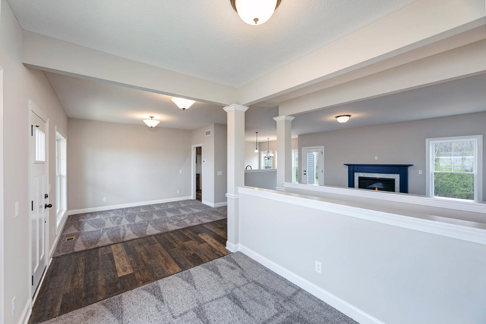 Living room with white walls, wood flooring, carpet, two fireplaces, white-framed window, ceiling light fixture, and tile accents