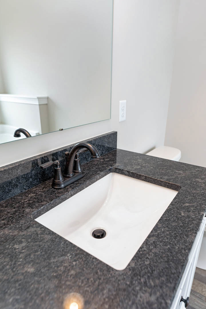 White rectangular sink with matte black faucet set against light tile backsplash and white countertop in modern bathroom.