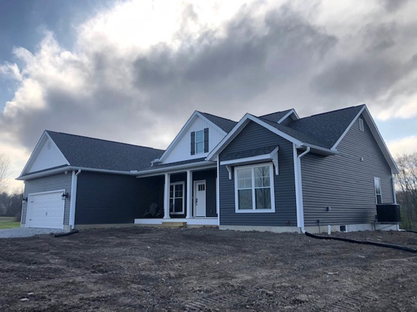 Two-story house with white siding, white-framed windows, attached white garage door, concrete driveway, and overcast sky