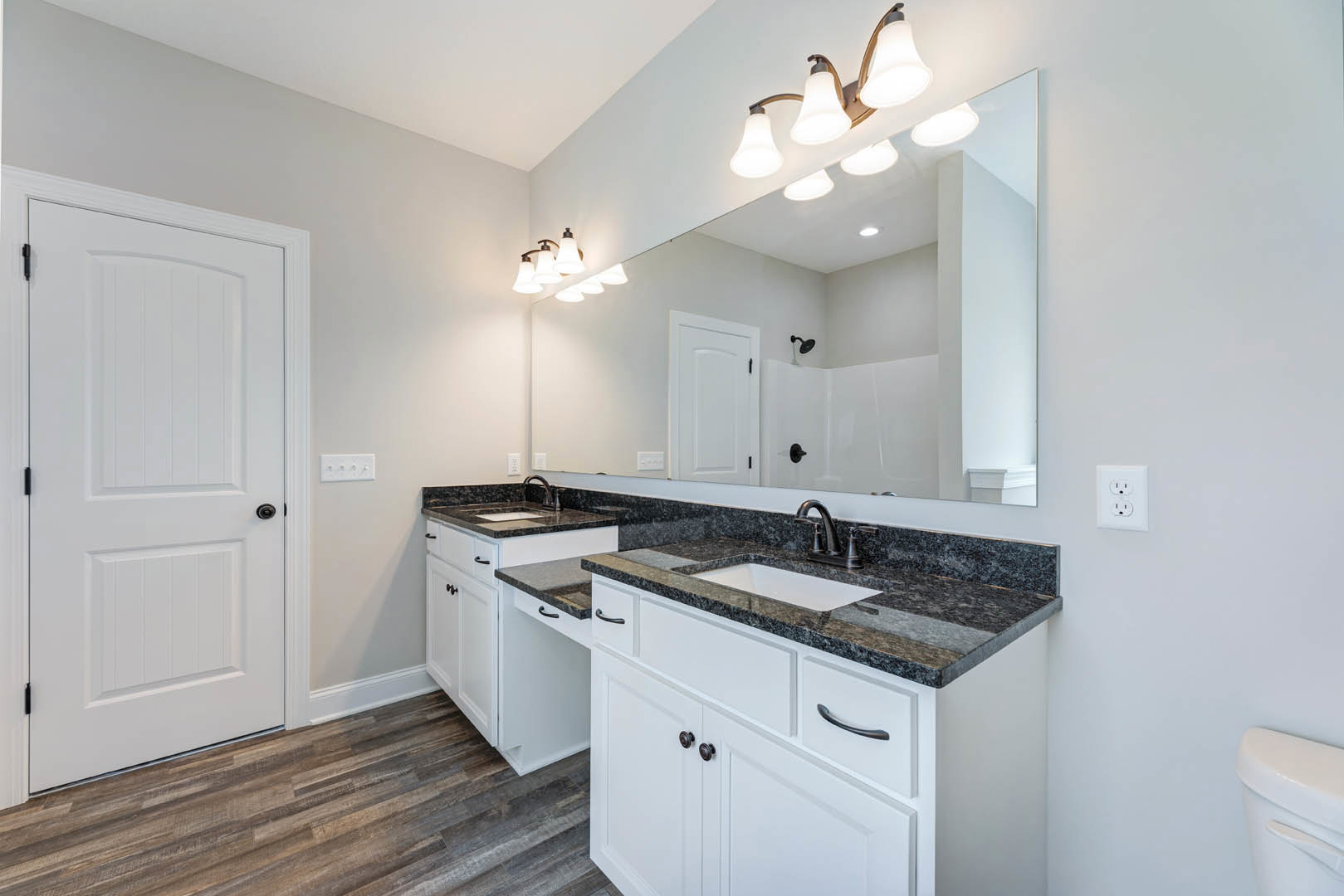 Bathroom with wide framed mirror above rectangular sink, white cabinetry with black hardware, quartz countertop, chrome faucet, wall-mounted light fixture, white door, and visible