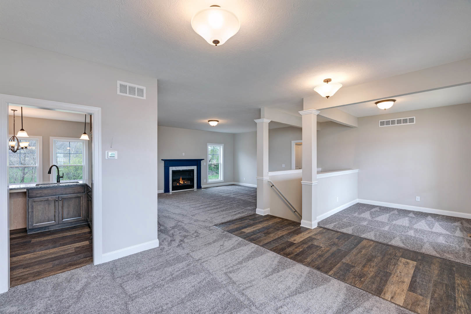Carpeted living area featuring a lit fireplace with white mantel, ceiling light fixture, white-framed window, built-in cabinetry, and ceiling vent.