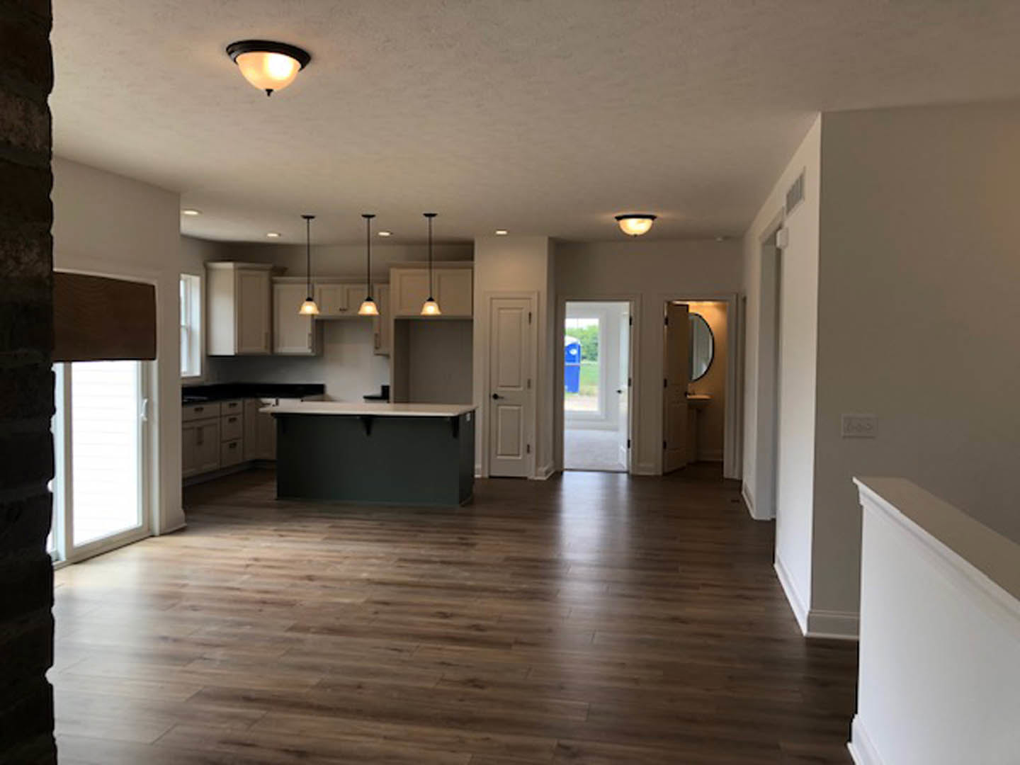 Open kitchen and dining area with wood flooring, white cabinetry, stone countertops, and a white door with black handle; blue container visible outside through glass door.