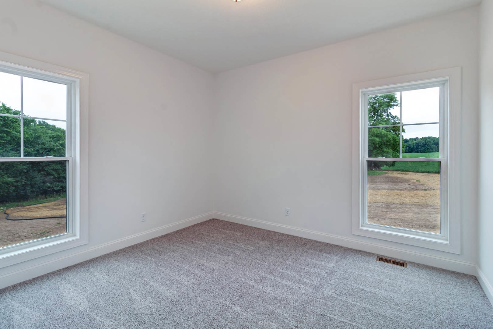 Carpeted room with white walls, large window showing blue sky, clouds, and green field with trees
