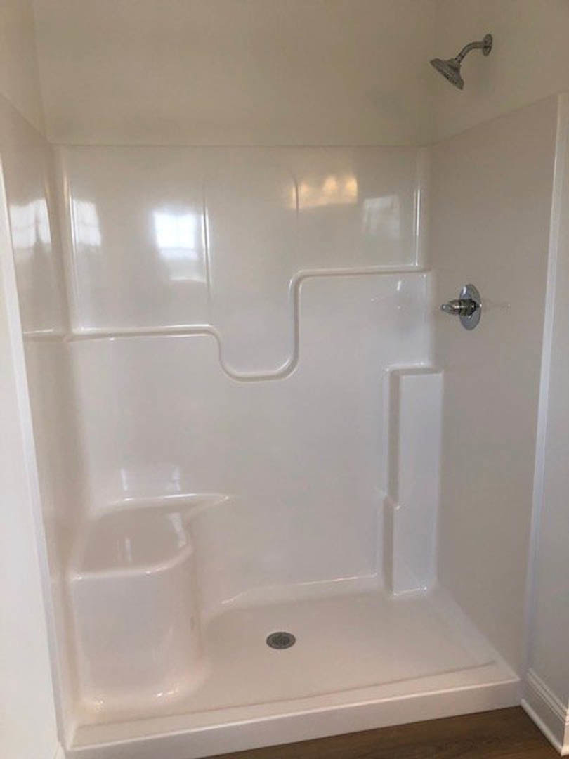 White tile shower with chrome shower head, built-in tub, and circular drain