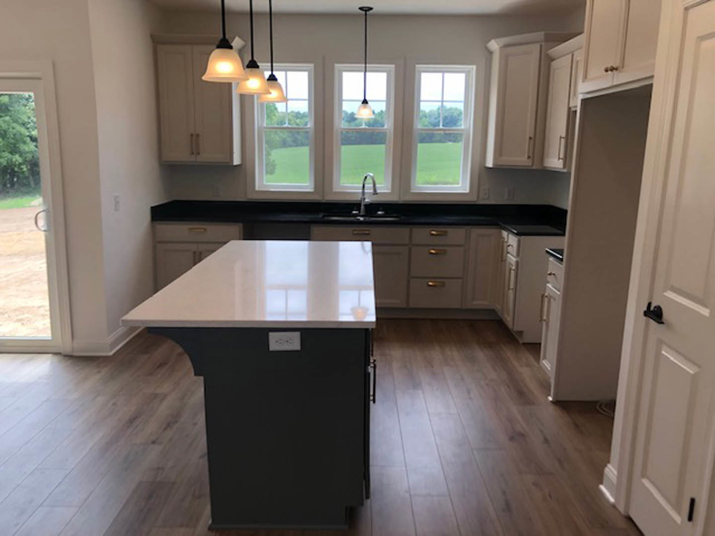 Modern kitchen featuring a central island with a white countertop, built-in sink, and power outlet; large windows provide natural light, white walls contrast with black