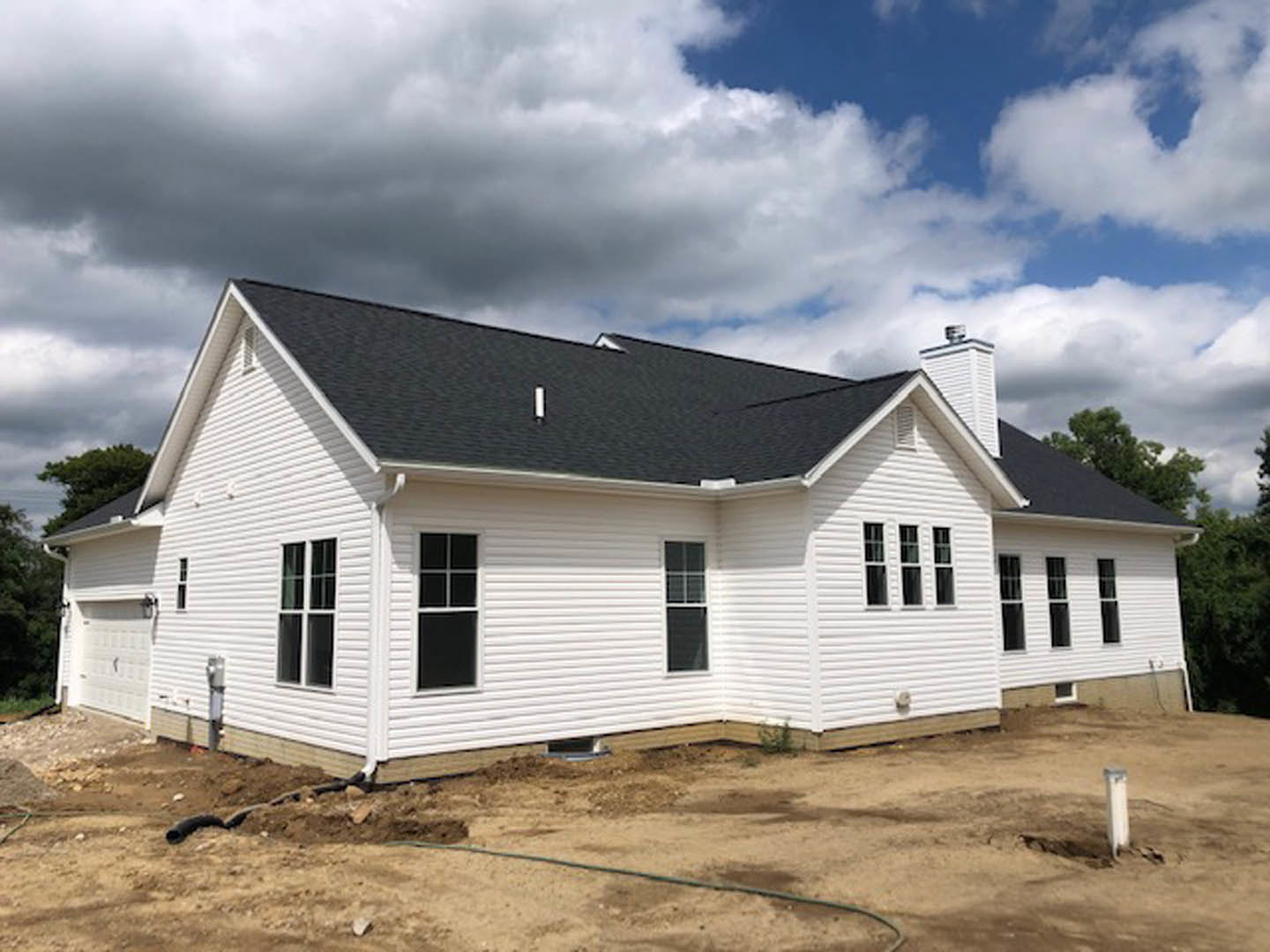 White house with black roof under construction, white-framed windows, dirt patch in front, cloudy sky, Robert Frost Farm visible in background