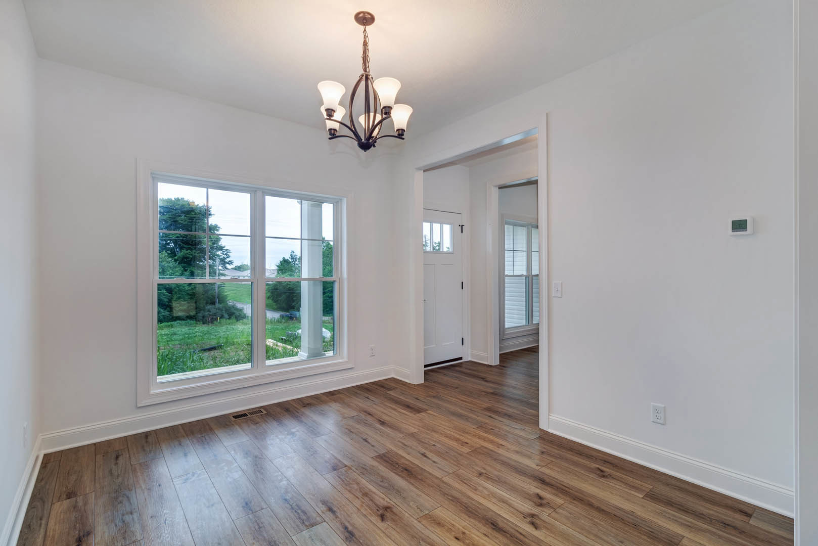 Hardwood floor room with white-light chandelier, large window overlooking grassy yard, white walls with crown molding