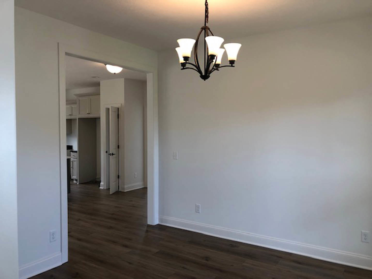 Chandelier with five lights hanging from white ceiling in a room with dark hardwood floor and white plaster walls; door visible in background.