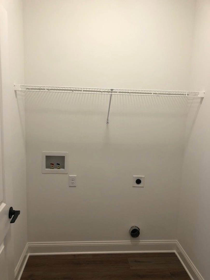 White closet with a white shelf, black door, and light wood floor