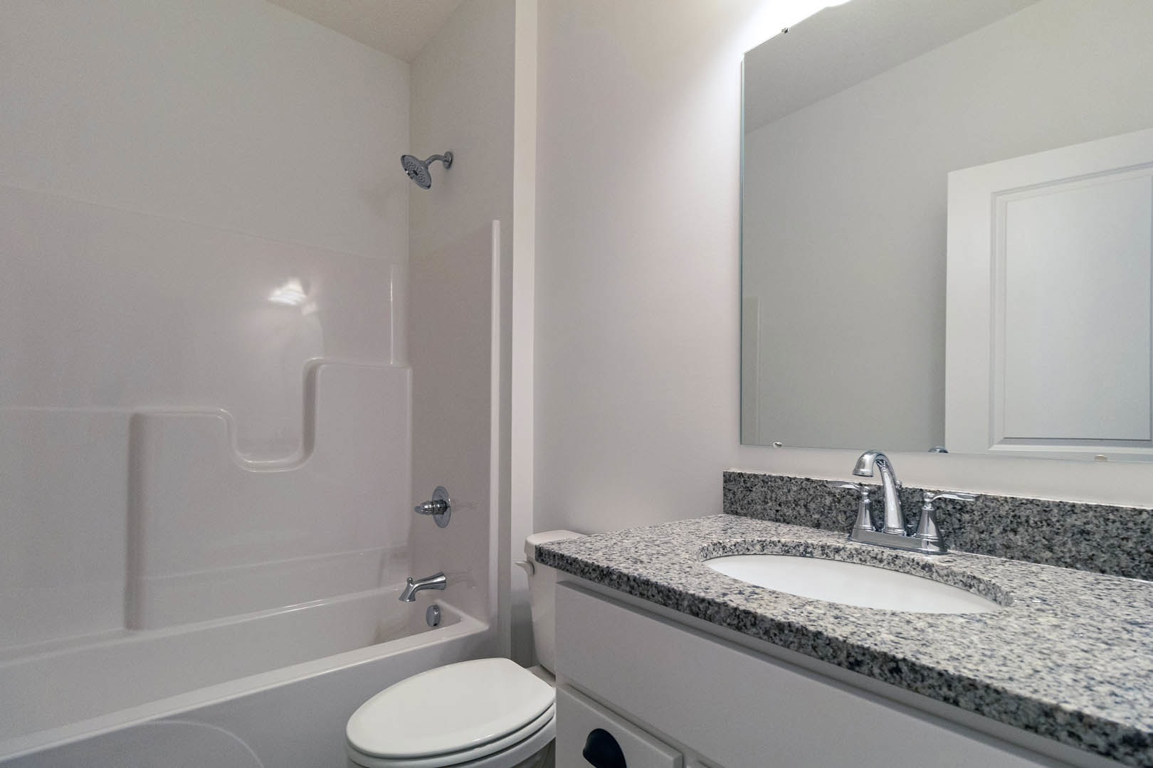 Bathroom with marble countertop sink, chrome faucet, white toilet, glass-enclosed shower, and light tile walls