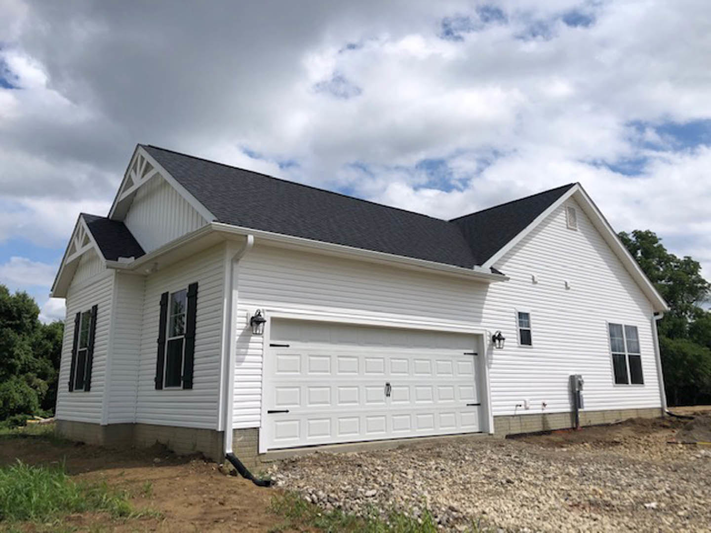 White siding house with attached garage, white framed windows, and shingled roof under partly cloudy sky
