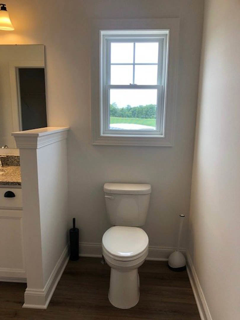 White toilet with closed lid beside a striped black and white accent wall, window overlooking grassy field, light-colored tile floor