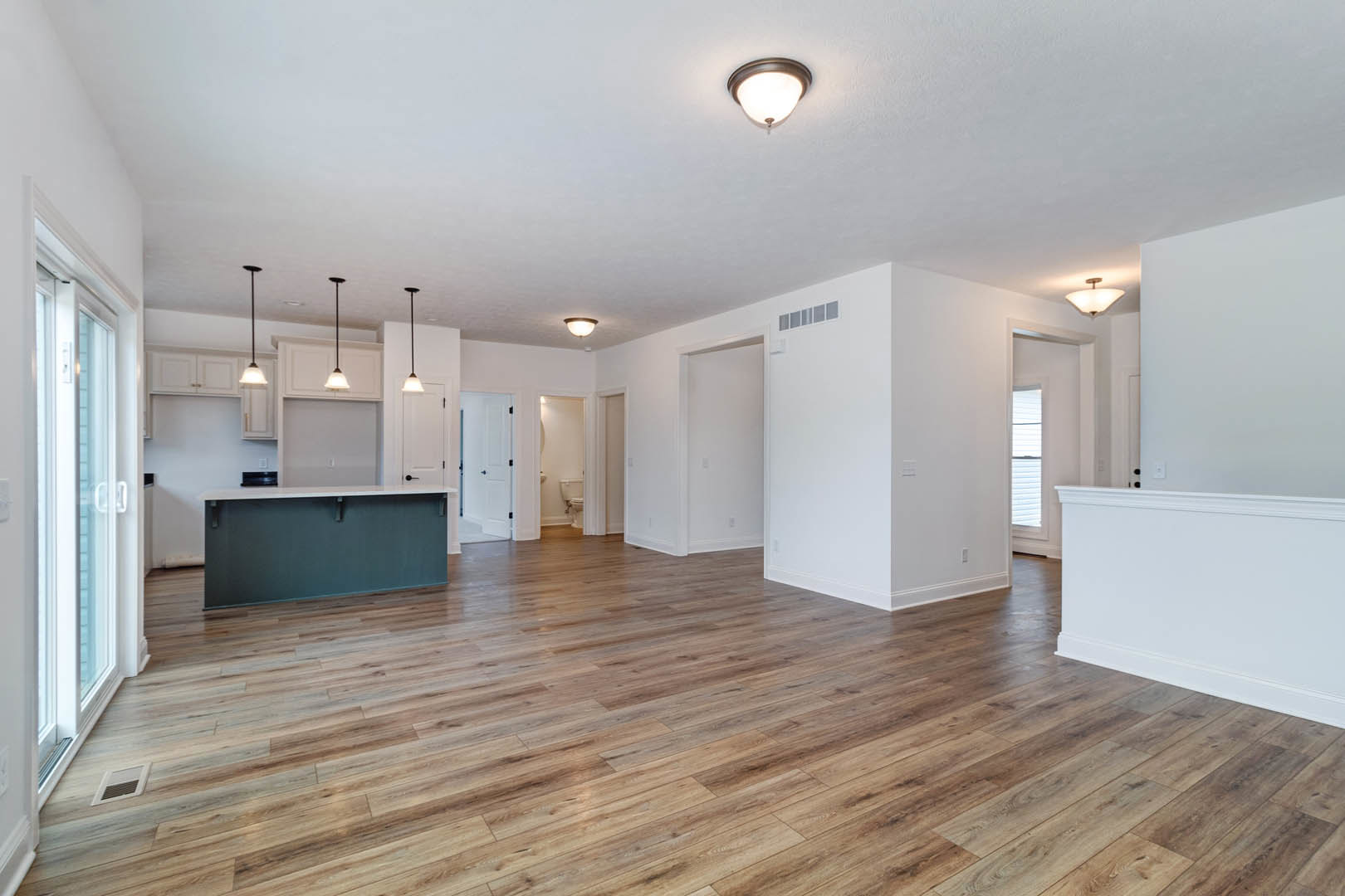 Open-concept kitchen and living area with wood flooring, white walls, glass door, ceiling light fixture, and vent