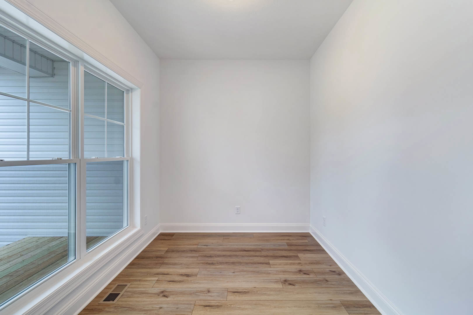 Sunlit room with large window, white walls, and polished wood flooring with white baseboard trim