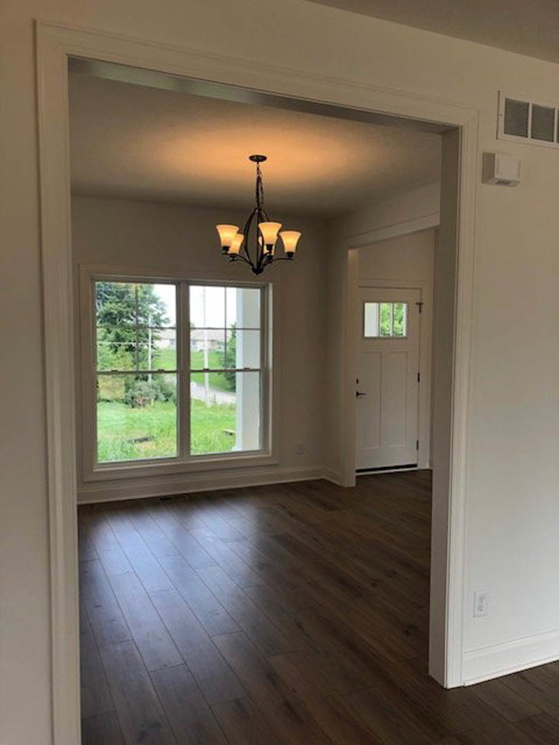 Room with dark wood flooring, white door with glass window, large window overlooking grassy yard, and multi-light chandelier hanging from ceiling