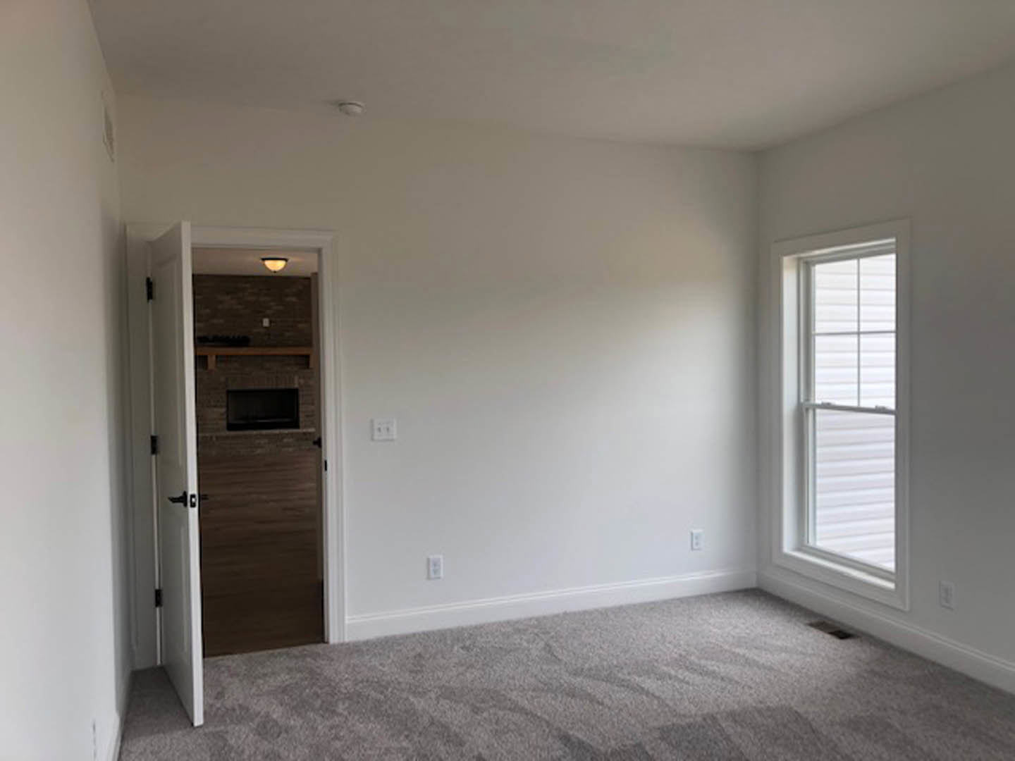 Open white door with silver handle leads to a carpeted room featuring a window with white trim and a fireplace surrounded by light-colored walls.