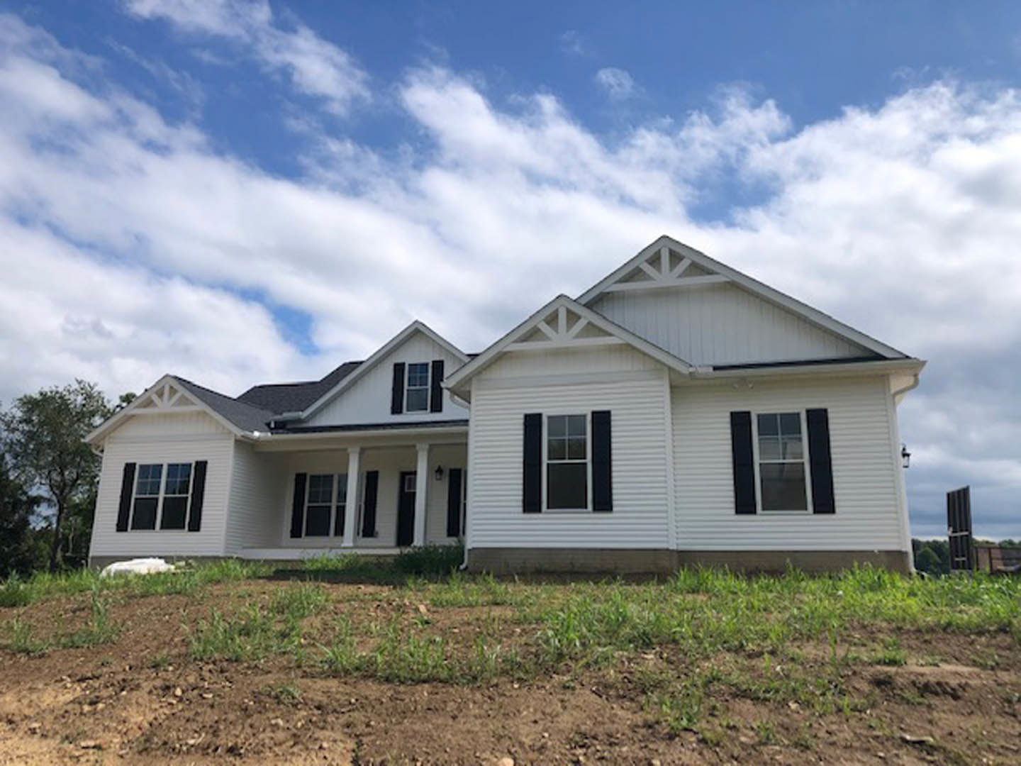 White siding house with black shutters, white-framed windows, manicured green lawn, blue sky with scattered clouds