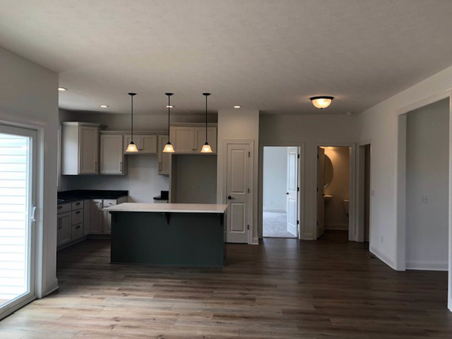 Open kitchen and dining area with white quartz countertop, wood flooring, white cabinetry, stainless steel sink, window with blinds, and white doors featuring black hardware.