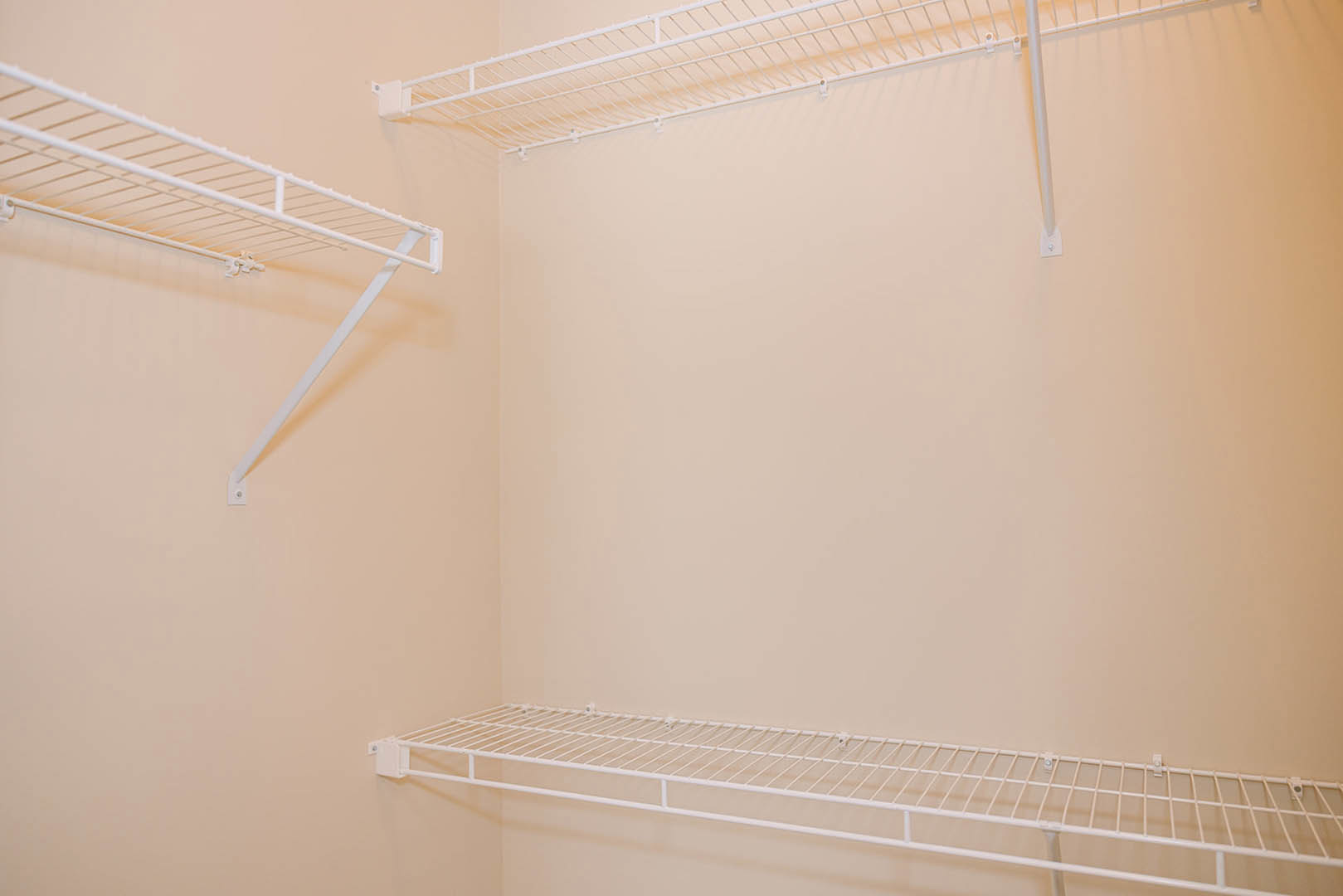 White wire shelving unit mounted on a white wall in a room, featuring metal rods and open storage.