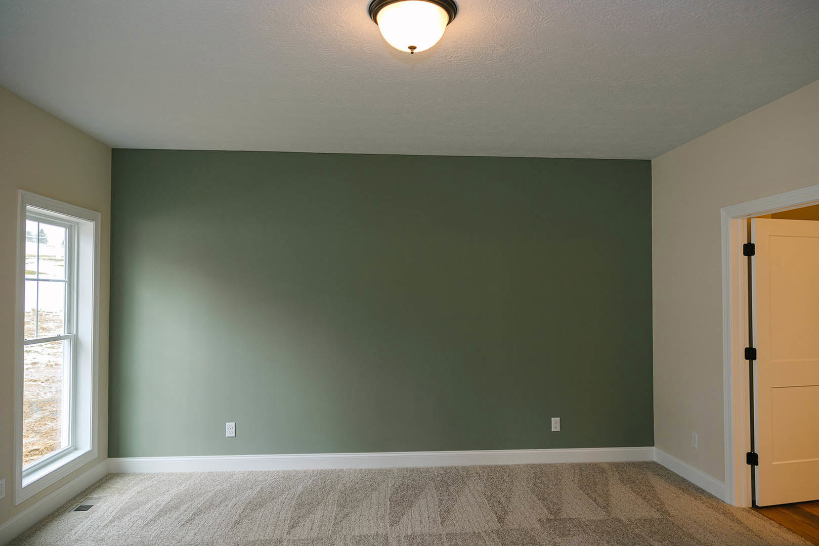 Bedroom with green accent wall, white ceiling, ceiling light fixture, black door handle on white door, large window, and beige carpet flooring