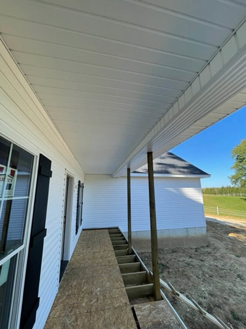 White house porch with white siding, white roof, wooden deck stairs, black railing, and shaded outdoor area.