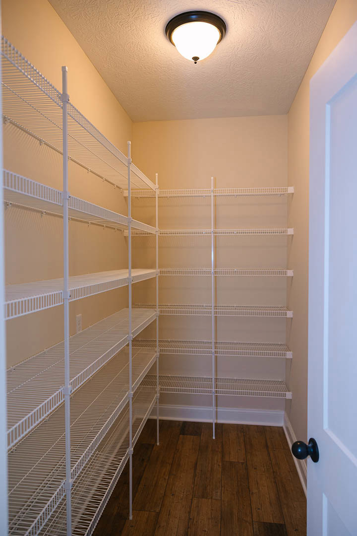Empty closet with built-in white shelves, wood flooring, ceiling light fixture, white walls, and a close-up of a door knob.