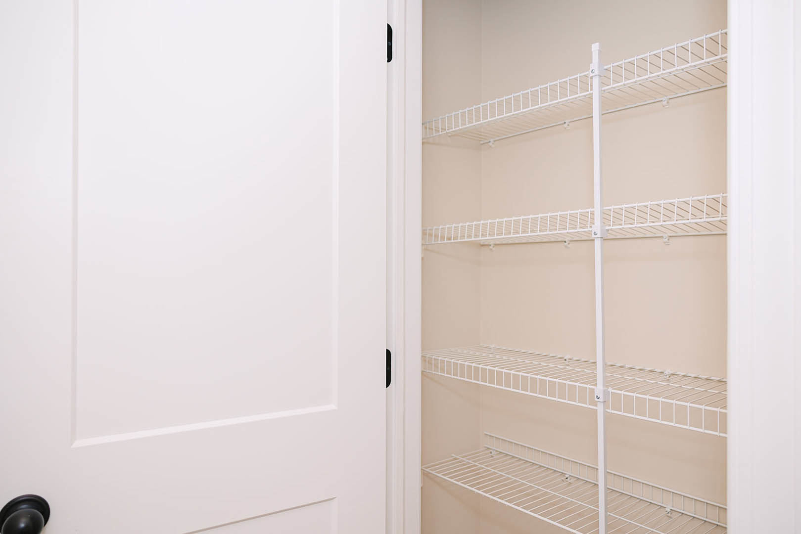 White wire shelving installed in a closet with white walls, a white door featuring a black handle, and a black object resting on one of the shelves.