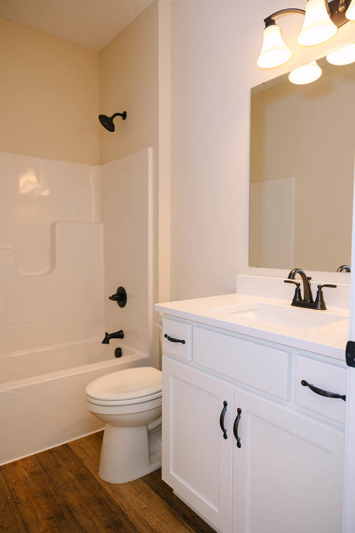 White bathroom featuring a black shower head mounted on tiled wall, modern toilet, black hardware on cabinetry, sleek faucet, and multi-bulb light fixture above sink.