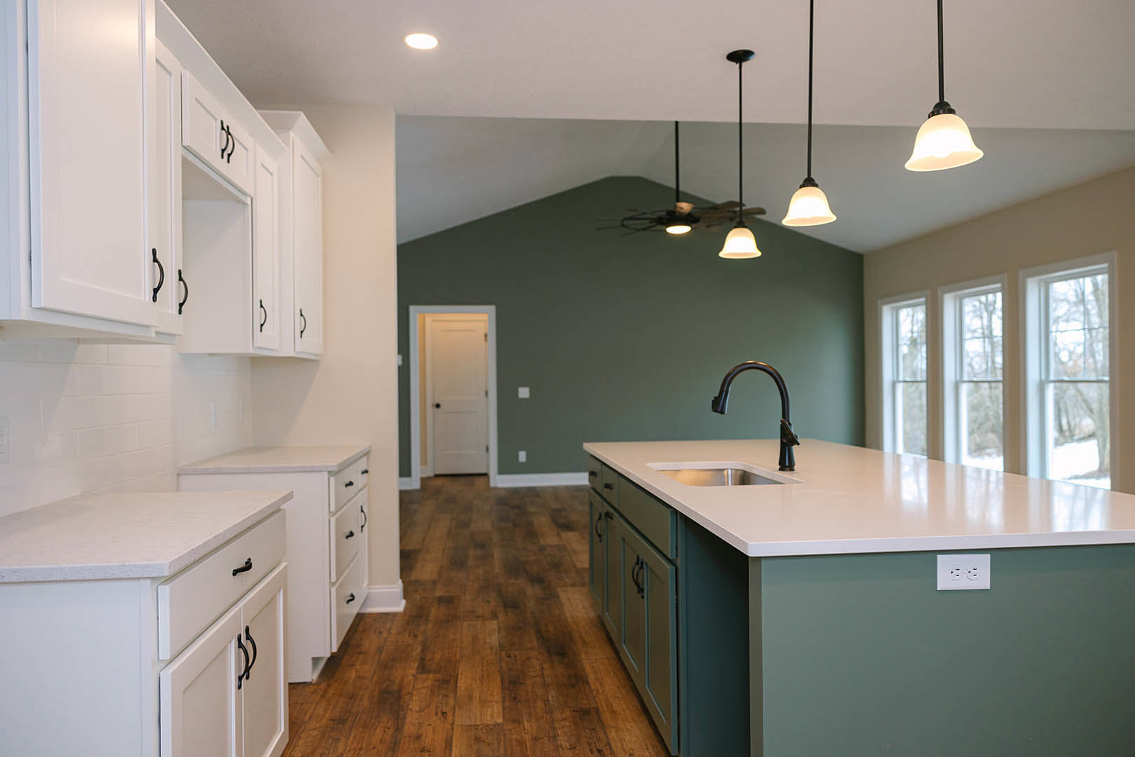 White kitchen cabinets, black faucet, white countertop with undermount sink, multiple windows, white door with black knobs, close-up of white electrical outlet, light-colored