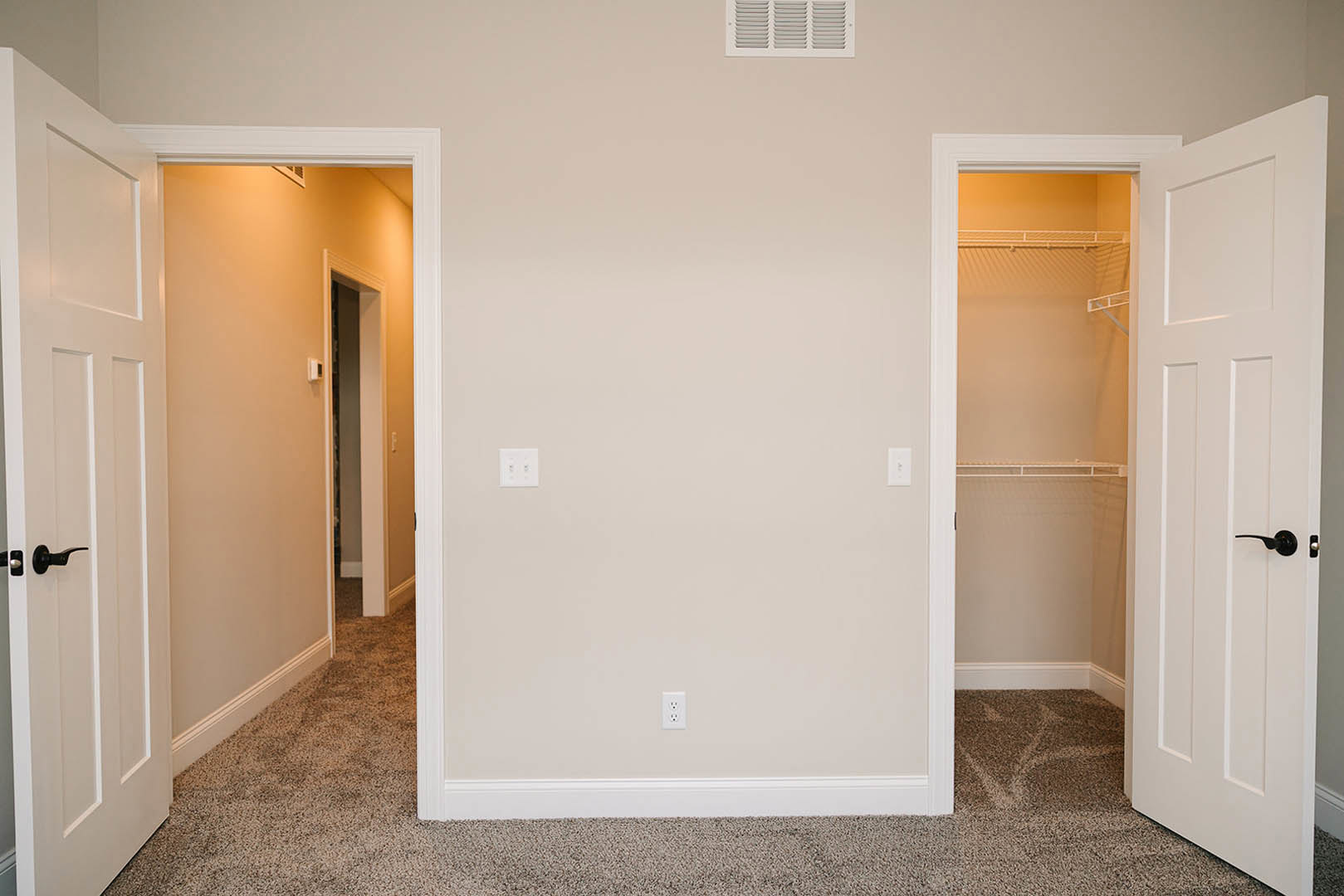 Open closet with carpeted floor, white bi-fold doors, close-up of brushed metal door handle, white wall outlet and switches, vent detail, red and white striped ceiling above white