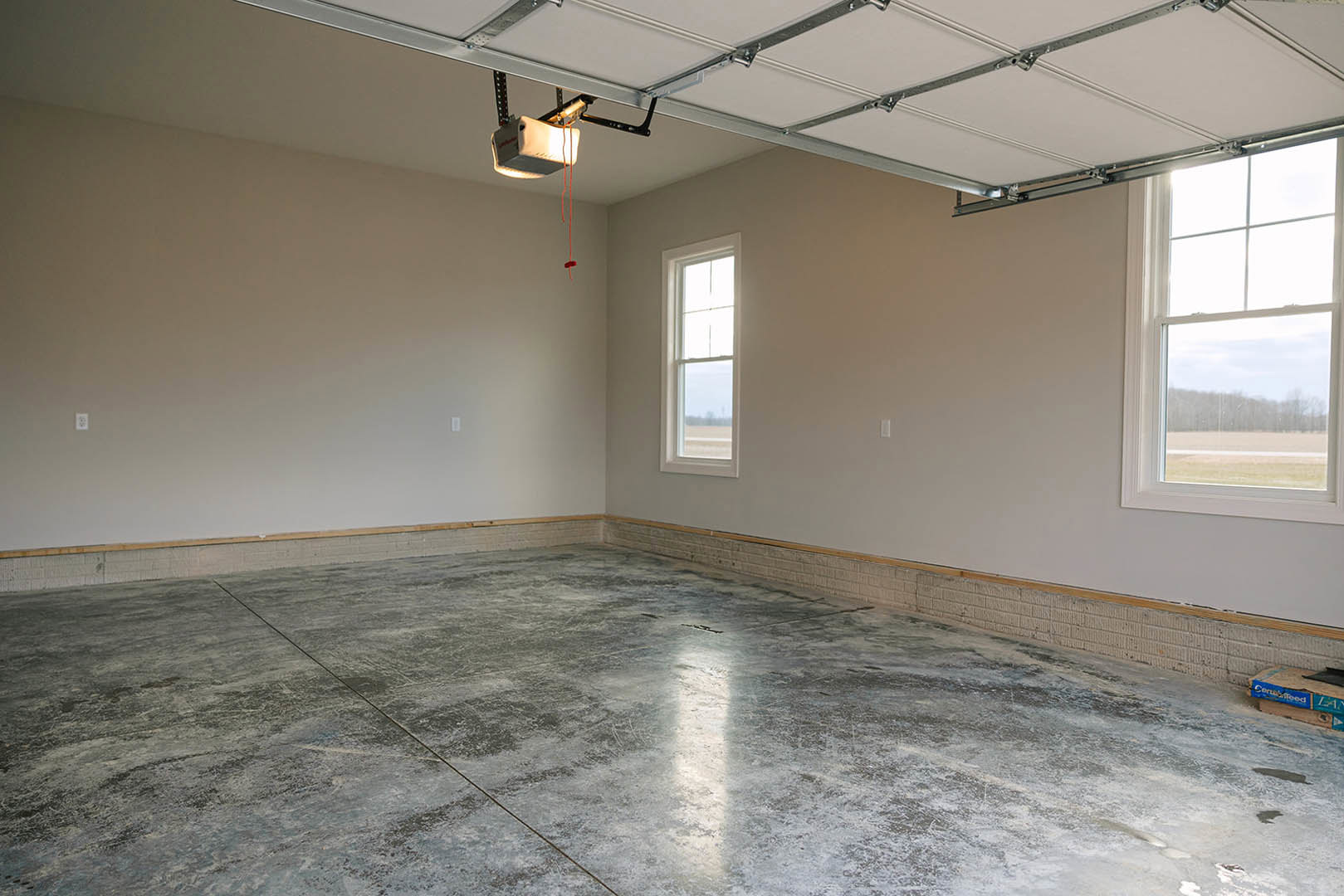 Modern room with polished concrete floor, plaster walls, large window offering outdoor view, blue storage box on wooden table, and metal-framed light fixture suspended from ceiling