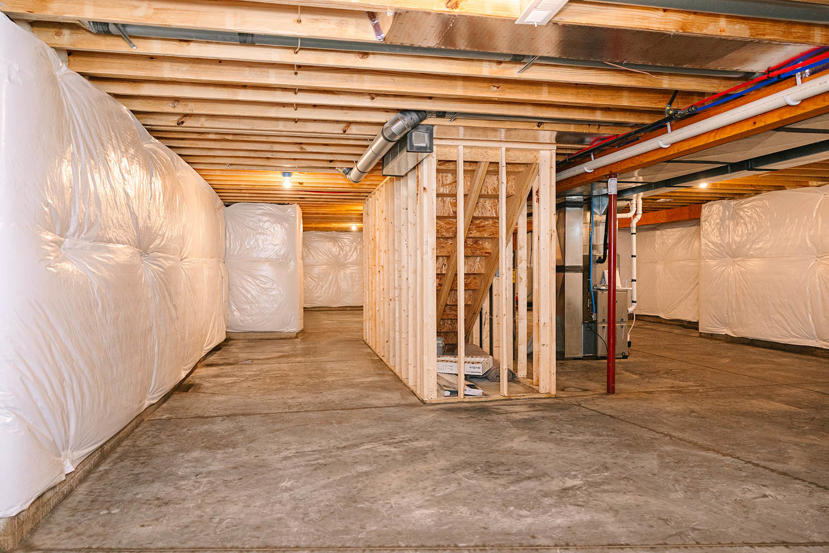 Basement room with unfinished wooden wall, exposed ceiling beams, concrete floor, white plastic bags, and a white mattress.
