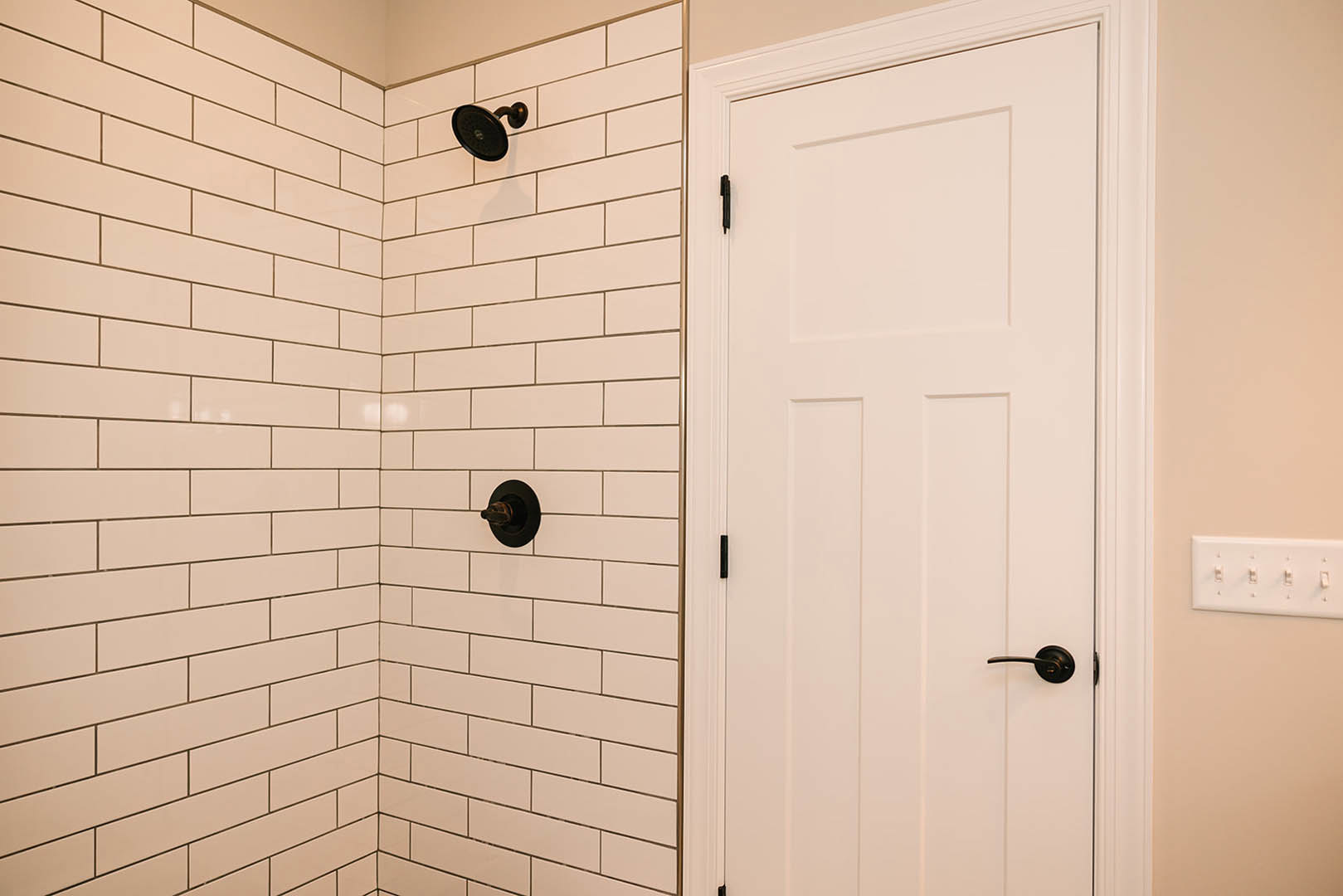 Frameless glass shower door with matte black handle, chrome shower head, and white subway tile wall