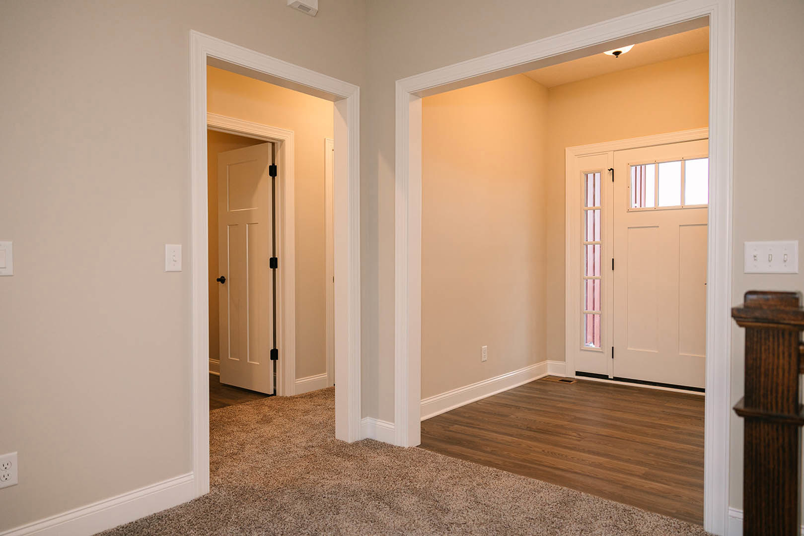 Hallway with white paneled doors, light wood flooring, white walls with molding, glass-paneled door, carpet runner, and built-in wooden shelf.